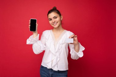 Moda kıyafetleri içinde genç, beyaz, hippi bir kadının portresi. Stüdyoda kırmızı duvarın yanında yalnız poz veren kaygısız seksi kadın. Doğal makyajlı pozitif bir model. Tutuluyor