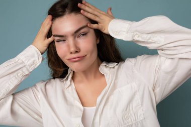 Çekici, eğlenceli, neşeli, pozitif, sevimli, sevimli, sevimli, genç, kıvırcık, esmer, beyaz tişörtlü, mavi arka planda yalnız bir kadın.