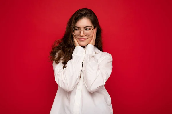 Attraktive junge lockige brünette Frau trägt weißes Hemd und optische Brille isoliert auf rotem Hintergrund mit leerem Raum — Stockfoto