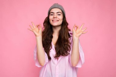 Fotokopi çekimli pembe arka planda izole edilmiş şık tişörtlü ve hippi gri şapkalı güzel, neşeli, neşeli, genç esmer kadın portresi.