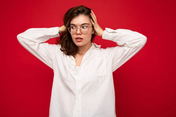 Schöne junge erstaunte lockige brünette Frau trägt weißes Hemd und optische Brille isoliert auf rotem Hintergrund mit Kopierraum. Schock-Konzept — Stockfoto