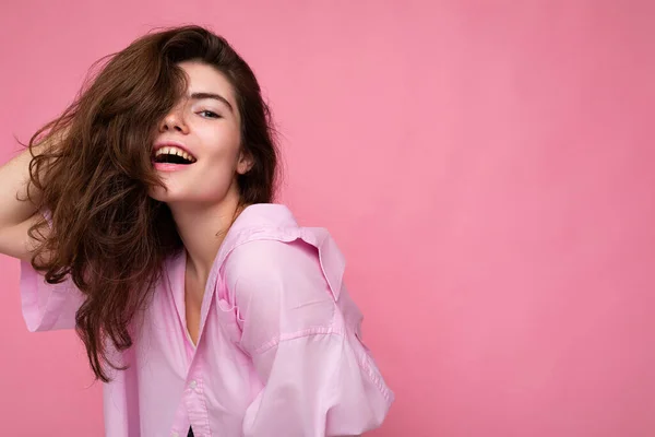 Retrato de bela sensual positiva jovem morena encaracolado usando camisa rosa e chapéu cinza isolado no fundo rosa com espaço de cópia — Fotografia de Stock