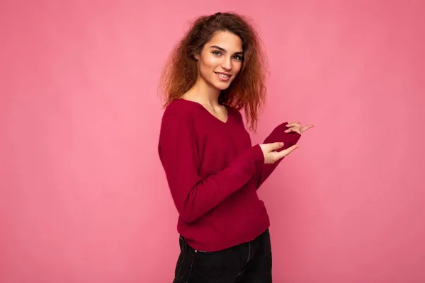 Foto van jonge vrolijke positieve glimlach mooie brunette golvende vrouw met oprechte emoties dragen casual roze trui geïsoleerd over roze achtergrond met kopieerruimte en wijzen naar lege ruimte voor — Stockfoto