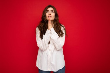 Beyaz gömlek giyen güzel, kıvırcık esmer kadının portresi. Kırmızı arka planda izole edilmiş. Fotokopi alanı olan, dua eden ve rüya gören.