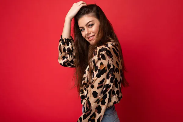 Foto de joven sonriente hermosa mujer morena sexy de moda con elegante blusa de leopardo aislada sobre fondo rojo con espacio vacío — Foto de Stock