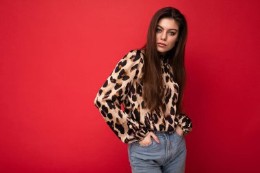 Hayvan desenli bluz giymiş güzel bir esmer kadın resmi. Kırmızı arkaplanda fotokopi alanı ile izole edilmiş poz veriyor.