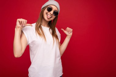 Genç, duygusal, pozitif, neşeli, neşeli, çekici, esmer, samimi duyguları olan, hippi kıyafetleri giyen, kırmızı arka planda izole edilmiş, fotokopi çeken ve kendini işaret eden bir kadının fotoğrafı.