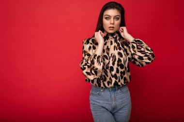 Hayvan desenli bluz giymiş güzel bir esmer kadın resmi. Kırmızı arkaplanda fotokopi alanı ile izole edilmiş poz veriyor.