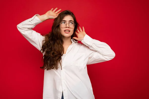 Aufnahme von attraktiven wütend traurig unzufrieden junge lockige brünette weibliche Person trägt weißes Hemd und optische Brille isoliert auf rotem Hintergrund mit freiem Raum — Stockfoto
