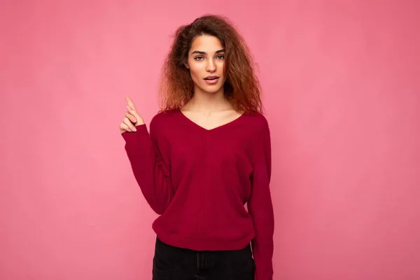Photo of young shocked beautiful brunette wavy woman with sincere emotions wearing casual pink sweater isolated over pink background with copy space and pointing at free space for mockup — Stock Photo, Image