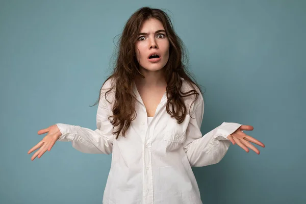 Attractive dissatisfied cute nice adorable tender young curly brunette woman wearing white shirt isolated on blue background with copy space — Stock Photo, Image