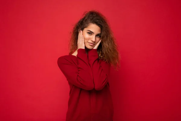 젊고 아름다운 곱슬곱슬 한 젊은 여성 이 캐주얼 한 붉은 스웨터를 입은 채 배경 벽에 고립된 진실 한 감정을 가지고 있다. 긍정적 인 개념 — 스톡 사진