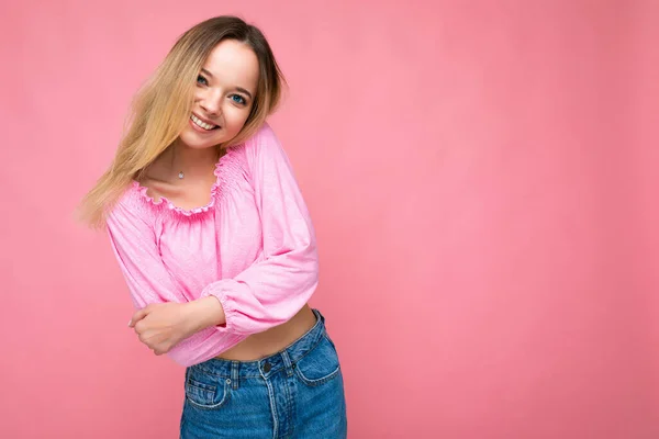 Portret van jonge mooie glimlachende hipster blonde vrouw in trendy roze gewas top blouse. Sexy zorgeloze vrouwelijke persoon poseren geïsoleerd in de buurt van roze muur in de studio. Positief model met natuurlijke make-up. Begrepen. — Stockfoto