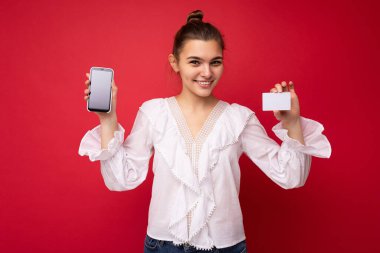 Beyaz bluz giyen, güzel Avrupalı, şık esmer bir kadın ve kırmızı arka planda izole edilmiş, samimi duygularla izole edilmiş şık bir şapka. Basit ve doğal bir şekilde kameraya bakıyor. Tutuluyor