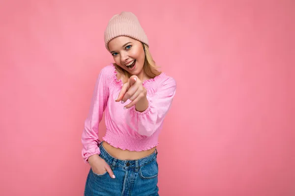 Foto van jonge positieve gelukkige mooie blonde vrouw met oprechte emoties dragen roze blouse en roze hoed geïsoleerd op roze achtergrond met kopieerruimte en wijzen naar camera — Stockfoto