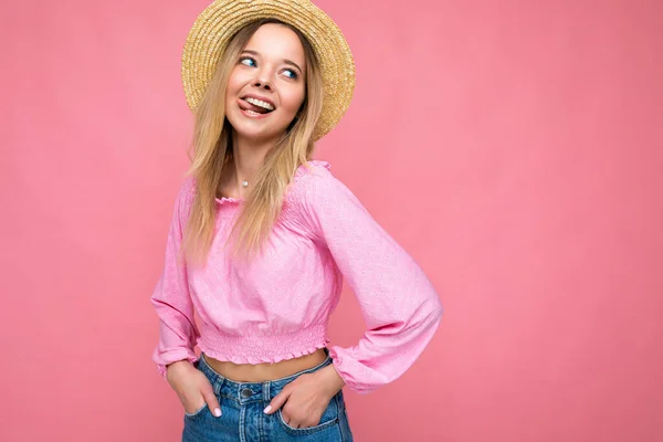 年轻迷人的嬉皮士金发女人穿着时髦的粉色庄稼顶盖和草帽的画像。性感无忧无虑的女性在工作室粉红墙壁附近摆出孤立无援的姿势。具有自然的正面模式 — 图库照片