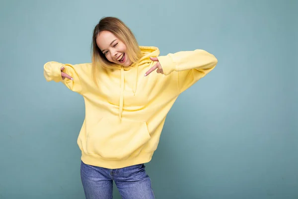 Foto de joven hermosa linda mujer rubia feliz con sudadera con capucha amarilla con estilo aislado sobre fondo azul con espacio de copia —  Fotos de Stock
