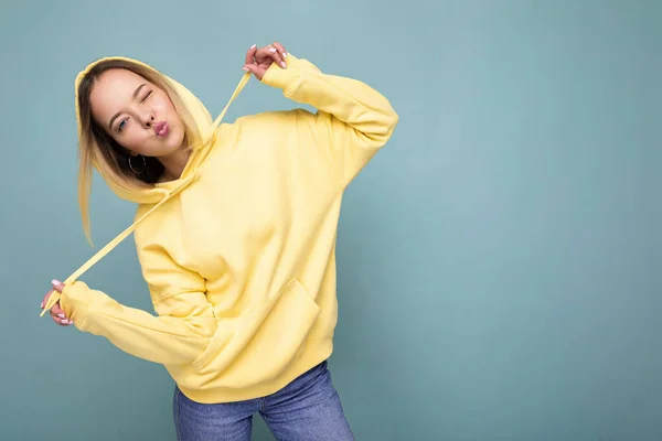 Foto de joven hermosa linda mujer rubia feliz con sudadera con capucha amarilla con estilo aislado sobre fondo azul con espacio de copia —  Fotos de Stock