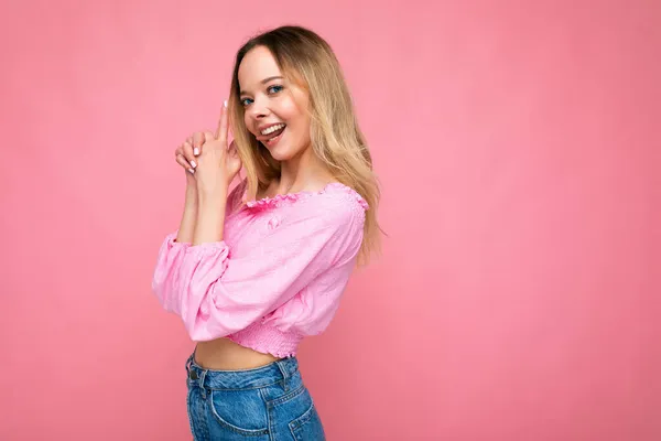 Фото молодой позитивной счастливой привлекательной блондинки с искренними эмоциями носить розовую блузку изолированы на розовом фоне с пустым пространством и изготовления пальца пистолет — стоковое фото