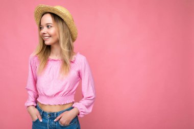 Pembe yaz bluzu ve modaya uygun hasır şapkalı güzel bir kadın. Pozitif kadın yüz duyguları gösterir. Pembe arka planda izole edilmiş, boş alanı olan komik bir model