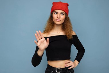 Kendine güveni tam, hoş, çekici, kumral, samimi duyguları olan, siyah bluz giyen, mavi arka planda izole edilmiş kırmızı şapkalı bir kadın.