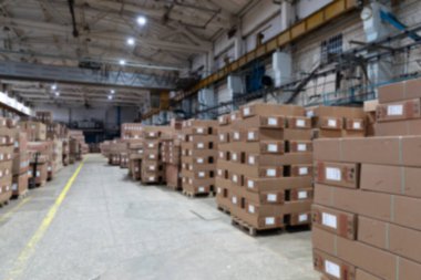 Büyük bir depo dolusu bitmiş ürün, paletlerin üzerindeki karton kutular, bulanık fotoğraf.