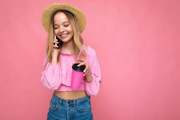 快乐的年轻女人一边用手机聊天一边用粉色背景喝咖啡 — 图库照片