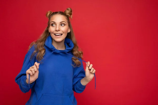 Φωτογραφία του νεαρού γοητευτικό όμορφο ελκυστικό χαρούμενο χαμόγελο ευχάριστο ξανθιά γυναίκα με δύο κέρατα με ειλικρινή συναισθήματα φορώντας κομψό hipster μπλε hoodie απομονώνονται σε κόκκινο φόντο με αντίγραφο χώρο — Φωτογραφία Αρχείου
