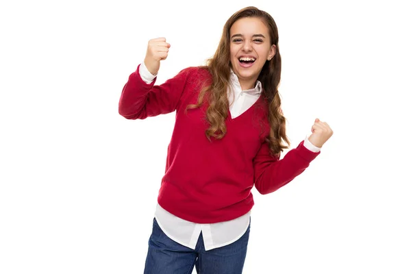 Φωτογραφία από όμορφο χαριτωμένο γοητευτικό χαμογελαστό ευτυχισμένη μελαχρινή έφηβη κοπέλα με μακριά μαλλιά σε κομψό κόκκινο πουλόβερ και λευκό πουκάμισο γιορτάζει τη νίκη απομονώνονται σε λευκό φόντο με ελεύθερο χώρο για κείμενο — Φωτογραφία Αρχείου