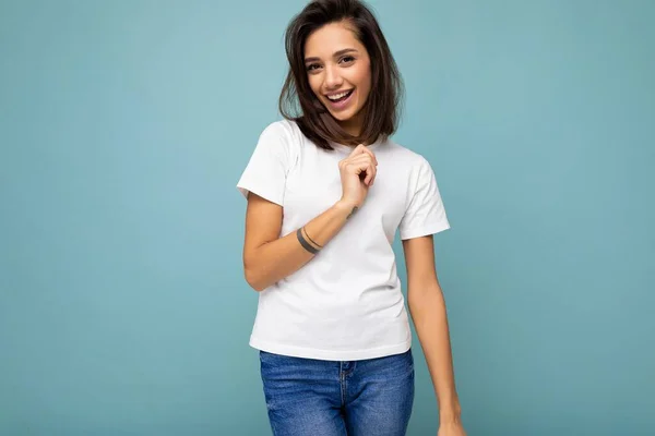 Портрет позитивной веселой улыбчивой молодой брюнетки в повседневной белой футболке для макета изолирован на синем фоне с копировальным пространством — стоковое фото
