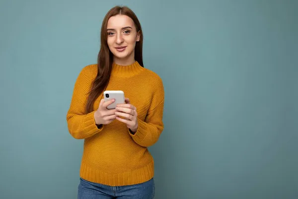 Atrakcyjnie wyglądająca młoda kobieta w stylowym stroju, odizolowana na tle z pustą przestrzenią, trzymająca się za ręce i korzystająca z sms-ów z telefonu komórkowego patrzących na kamerę. — Zdjęcie stockowe