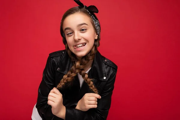 Photo shot of pretty positive smiling brunette little female teenager with pigtails wearing stylish black leather jacket and white t-shirt standing isolated over red background wall looking at camera — Stock Photo, Image