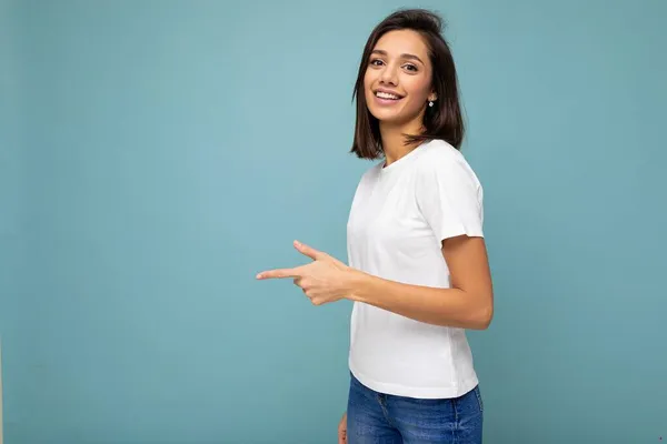 Foto de jovem positivo feliz sorrindo bela mulher com emoções sinceras vestindo roupas elegantes isoladas sobre fundo com espaço de cópia e apontando para o espaço livre — Fotografia de Stock