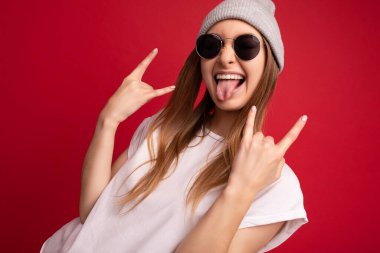 Genç, mutlu, neşeli, neşeli, gülen, güzel, esmer, beyaz tişörtlü, model, gri şapkalı ve güneş gözlüklü bir kadının portresi.