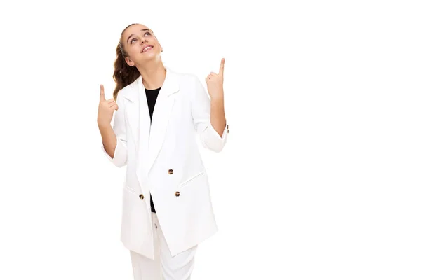 Foto von einem schönen netten entzückenden lächelnden brünetten Teenager-Mädchen mit Pferdeschwanz in einer stilvollen weißen Jacke und weißen Hosen isoliert auf weißem Hintergrund zeigt einen Finger nach oben auf einem freien Platz für Text — Stockfoto