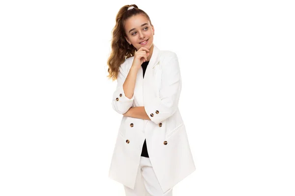 Foto de hermosa linda adorable positivo sonriente pensamiento morena adolescente con cola de caballo en elegante chaqueta blanca y pantalones blancos aislados sobre fondo blanco con espacio de copia para el texto — Foto de Stock