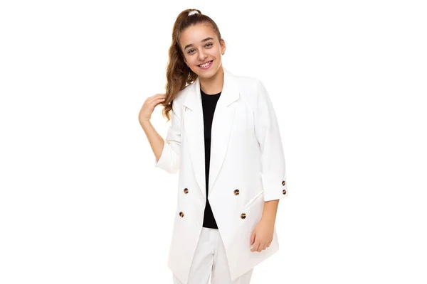 Foto van mooie schattige positieve glimlach brunette tienermeisje met paardenstaart in stijlvolle witte jas en witte broek geïsoleerd op witte achtergrond met kopieerruimte voor tekst — Stockfoto