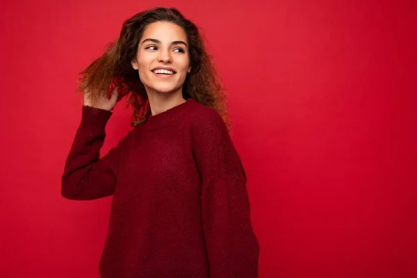 Fotografie krásné atraktivní mladé brunetky kudrnaté žena na sobě stylový tmavě červený svetr izolované přes červené pozadí zeď s volným prostorem pro text — Stock fotografie