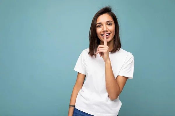 Foto de positivo feliz sorrindo jovem fascinante bonita atraente mulher morena agradável com emoções sinceras vestindo t-shirt branca casual para mockup isolado sobre fundo azul com espaço de cópia — Fotografia de Stock