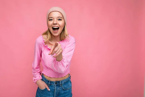 Fénykép a fiatal pozitív boldog ámulatba ejtett gyönyörű szőke nő őszinte érzelmek visel rózsaszín blúz és rózsaszín kalap elszigetelt rózsaszín háttér másolási hely és mutató ujját a kamera — Stock Fotó