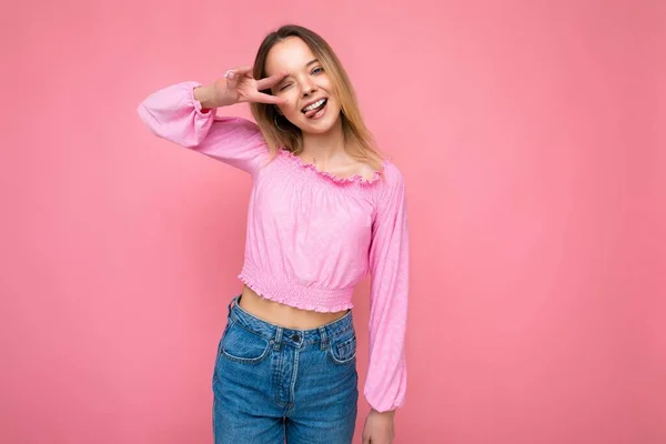 年轻迷人的笑容满面的嬉皮士金发女人穿着时髦的粉色麦穗上衣的画像。性感无忧无虑的女性在工作室粉红墙壁附近摆出孤立无援的姿势。正面模式 — 图库照片