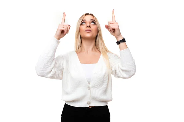 Photo of a beautiful attractive pretty amazing charming young blonde woman with makeup in a stylish white knitted sweater and black pants shows fingers up isolated on a white background with empty — Stock Photo, Image