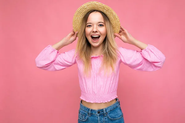 Фото фото молодой красивой милой счастливой блондинки, носящей стильный розовый топ и соломенную шляпу на розовом фоне с копировальным пространством — стоковое фото