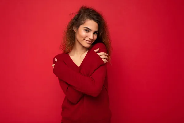 Приваблива позитивна молода кучерява брюнетка жінка з щирими емоціями, що отруюють ізольовані на фоні стіни з порожнім простором в повсякденному темно-червоному светрі. Щаслива концепція — стокове фото
