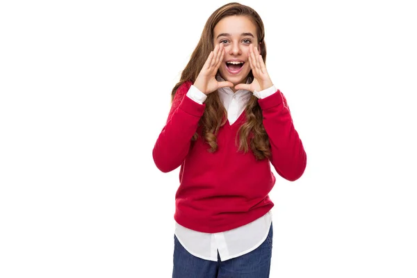 Photo of beautiful cute charming positive brunette teenage girl with long hair in stylish red sweater and white shirt shouts with open mouth isolated on white background with free space for text — Stock Photo, Image