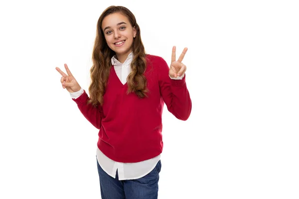 Foto de hermosa linda encantadora y sonriente chica adolescente morena con el pelo largo en suéter rojo elegante y camisa blanca muestra dos dedos aislados sobre fondo blanco con espacio libre para el texto. Paz. —  Fotos de Stock