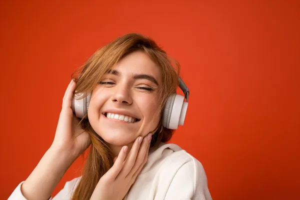 Close-up photo of beautiful happy smiling young blonde woman wearing white hoodie isolated over colourful background wall with copy space for text wearing white wireless bluetooth earphones listening — Stock Photo, Image