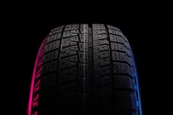 Schwarzer Reifen mit Lauffläche für die Fahrt auf Schnee auf schwarzem Hintergrund mit blau-roter Beleuchtung — Stockfoto