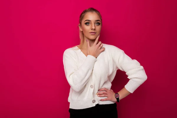 Foto de uma bela incrível mulher loira maravilhosa maravilhosa com maquiagem e rabo de cavalo em um elegante suéter de malha branca e calças pretas isoladas em um fundo rosa com espaço vazio para — Fotografia de Stock