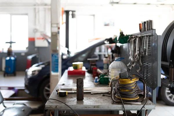 Foto eines Metalltisches mit Arbeitswerkzeugen zum Arbeiten und Reparieren eines Autos vor dem Hintergrund eines blauen Personenwagens an einer Tankstelle, der mit offener Motorhaube repariert wird — Stockfoto